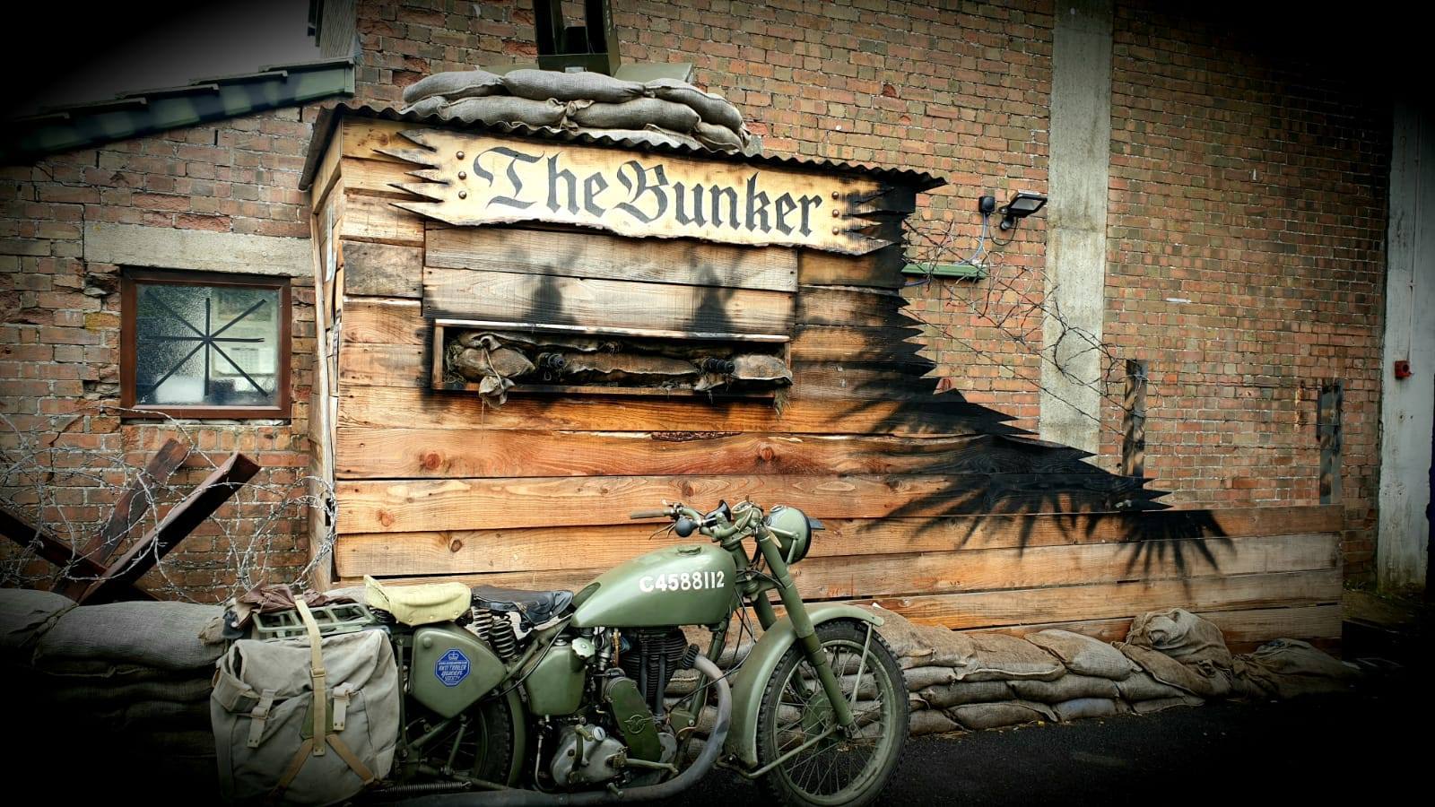 The Bunker's entrance: a sandbagged wooden hut with a WW2 motorcycle parked outside